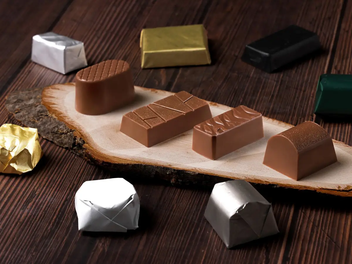 Chocolates wrapped in silver, gold, black and green foil beside unwrapped pieces, on a wooden slab